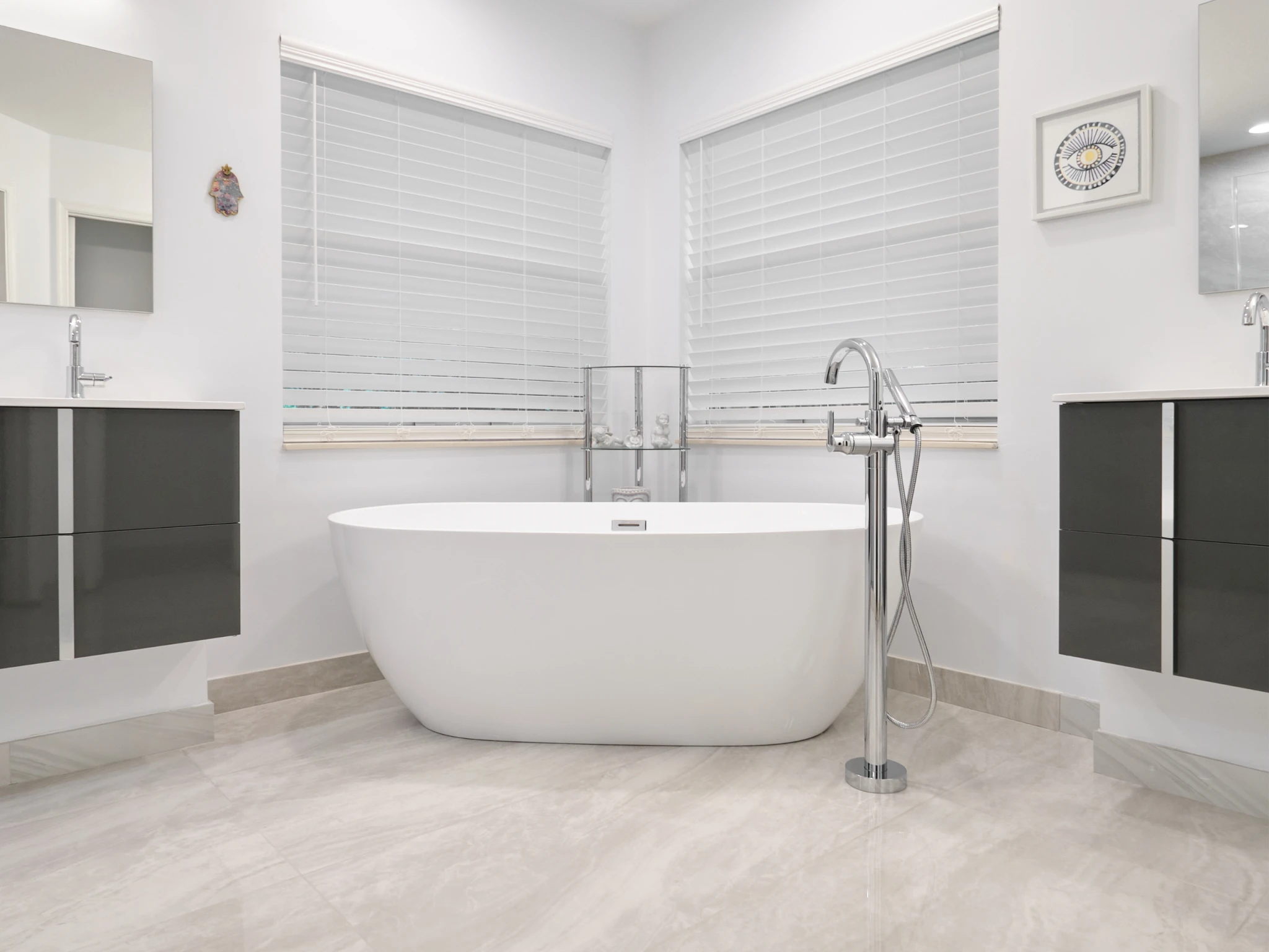 Modern bathroom remodeling with freestanding tub, dual vanities, white blinds, and light tile floor.