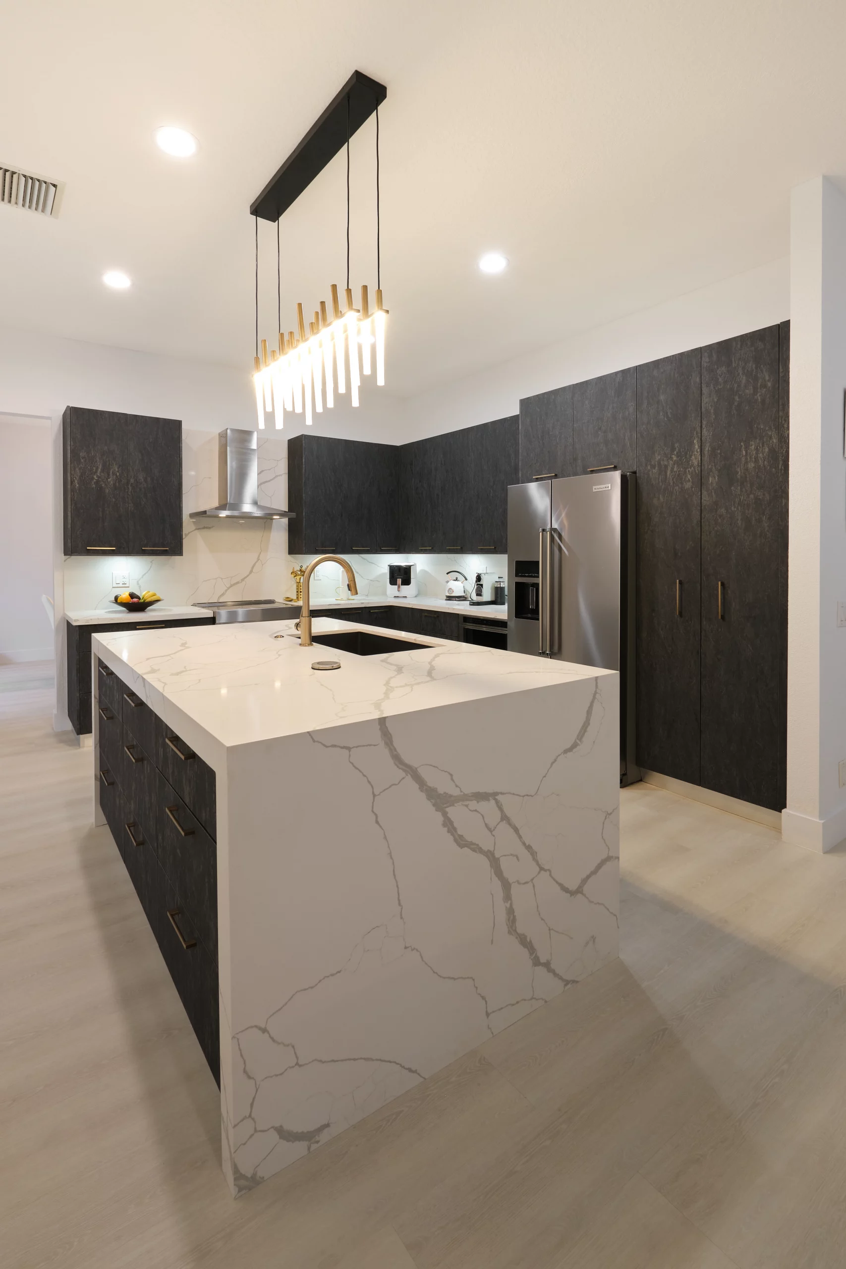 Modern kitchen remodeling with dark textured cabinets, white quartz island, and gold faucet.