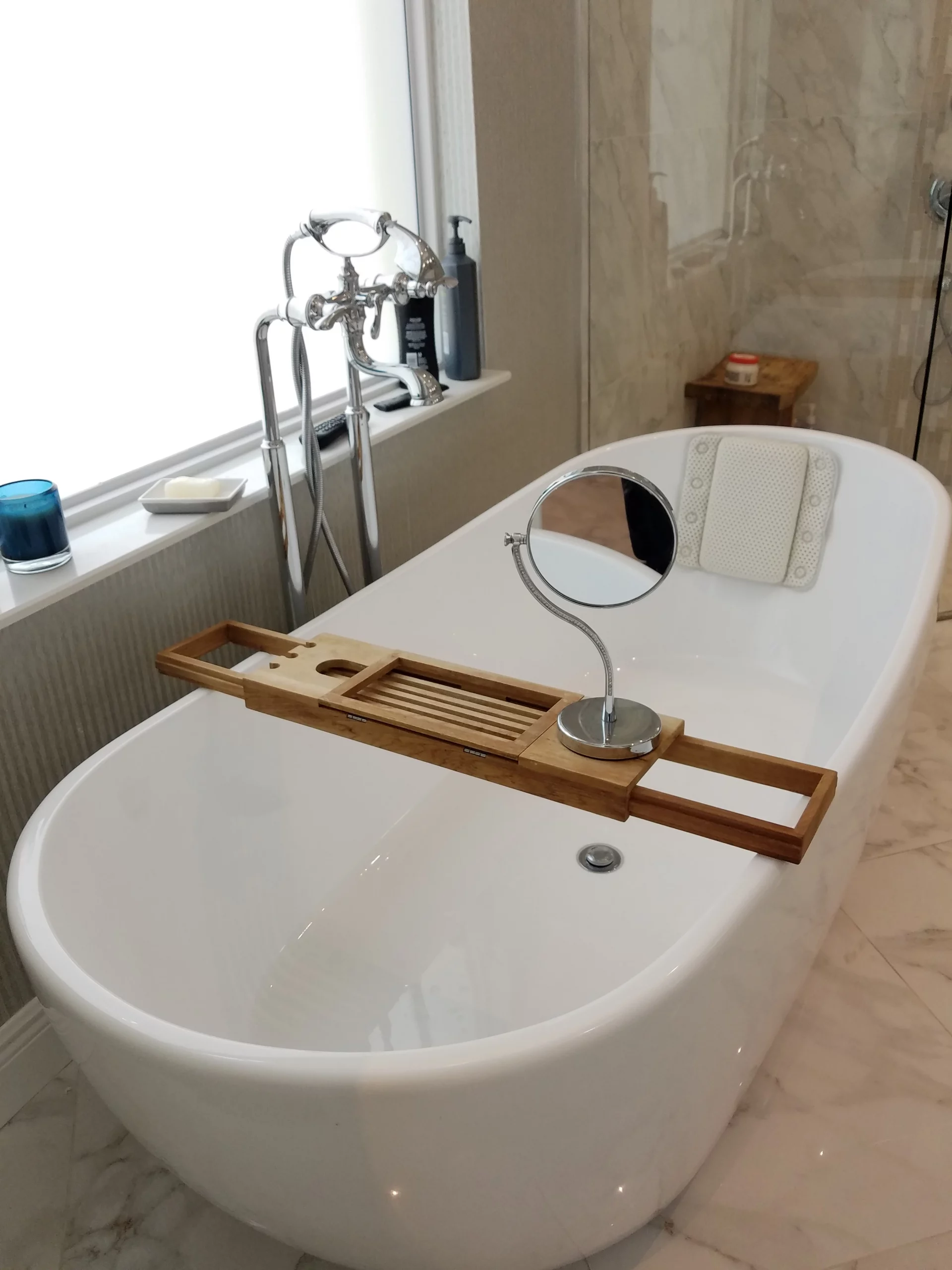 Freestanding bathtub setup with a wooden caddy and magnifying mirror, part of an elegant marble bathroom remodeling project.