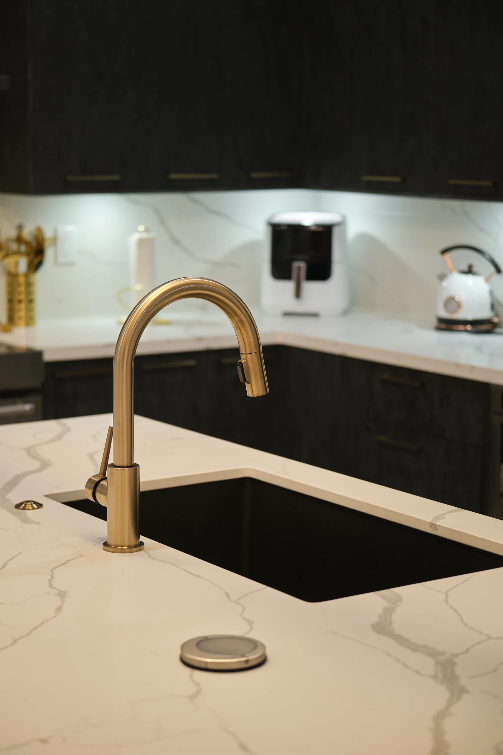 Close-up of a brushed gold kitchen faucet over a black sink in a modern kitchen remodeling.