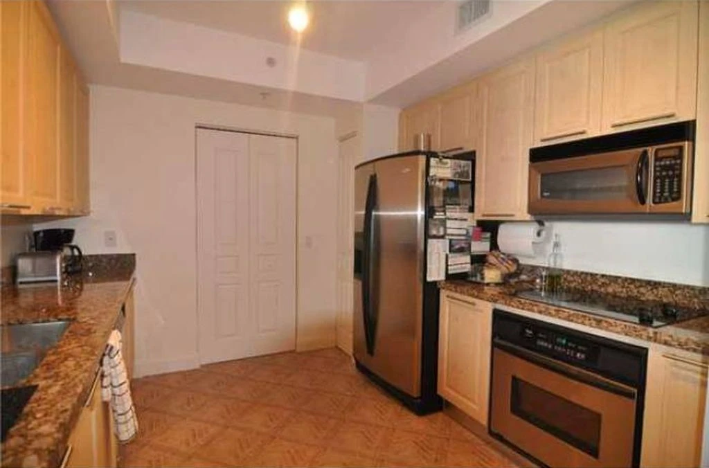 Before photo of a kitchen remodeling project featuring stainless steel appliances and light wood cabinets.