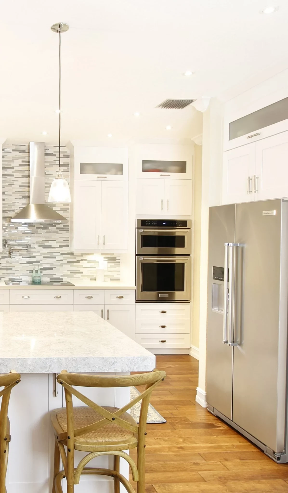 Bright transitional kitchen remodel featuring white shaker cabinets, stainless steel appliances, and wood bar stools.