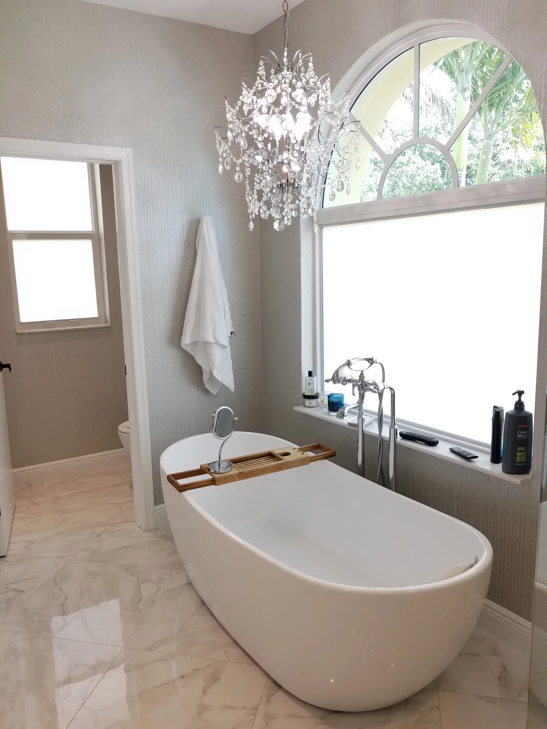 Freestanding tub in an elegant bathroom remodeling with marble floors and crystal chandelier.