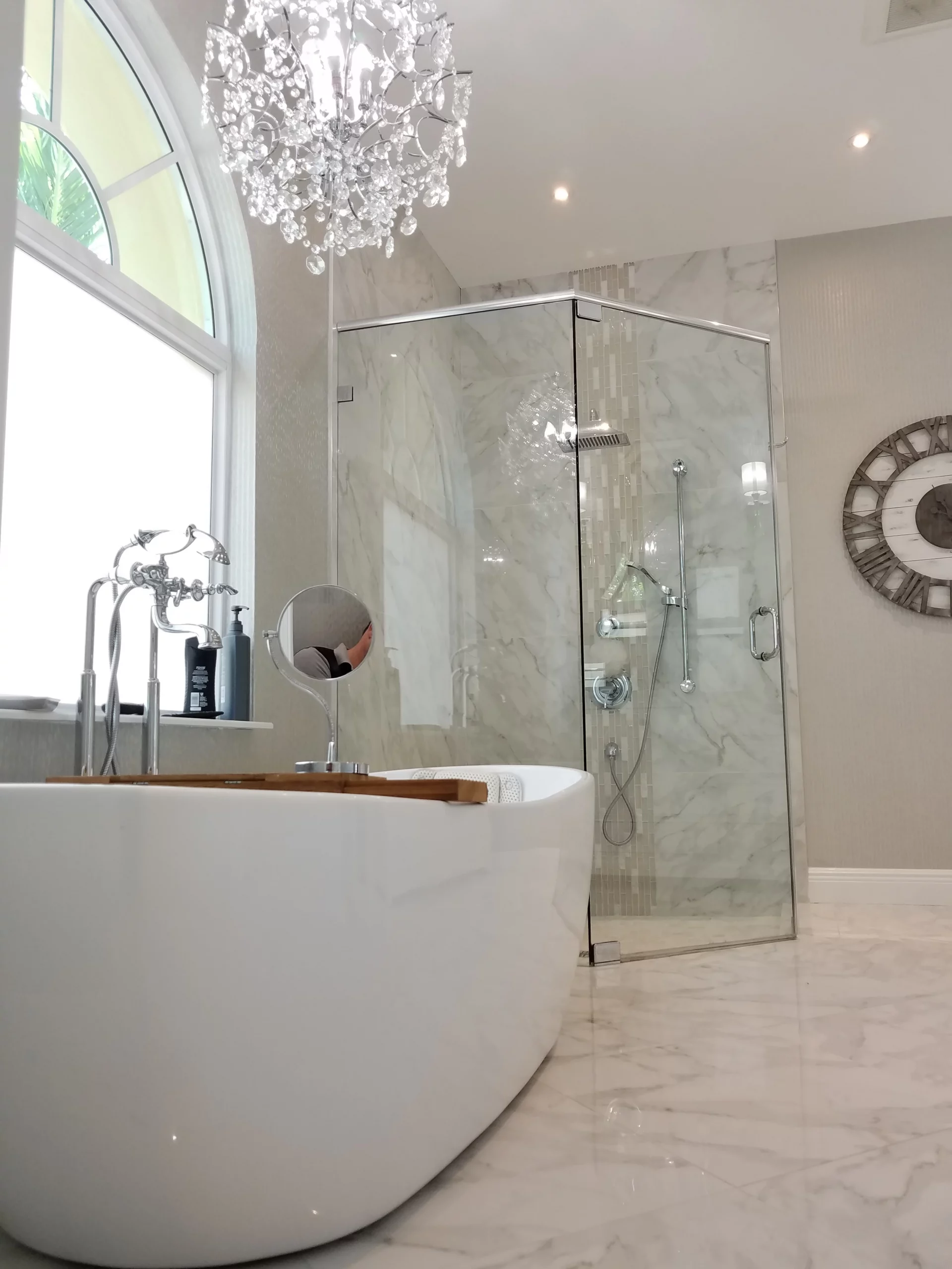 Luxurious bathroom remodeling featuring a white soaking tub, marble shower, and crystal chandelier.