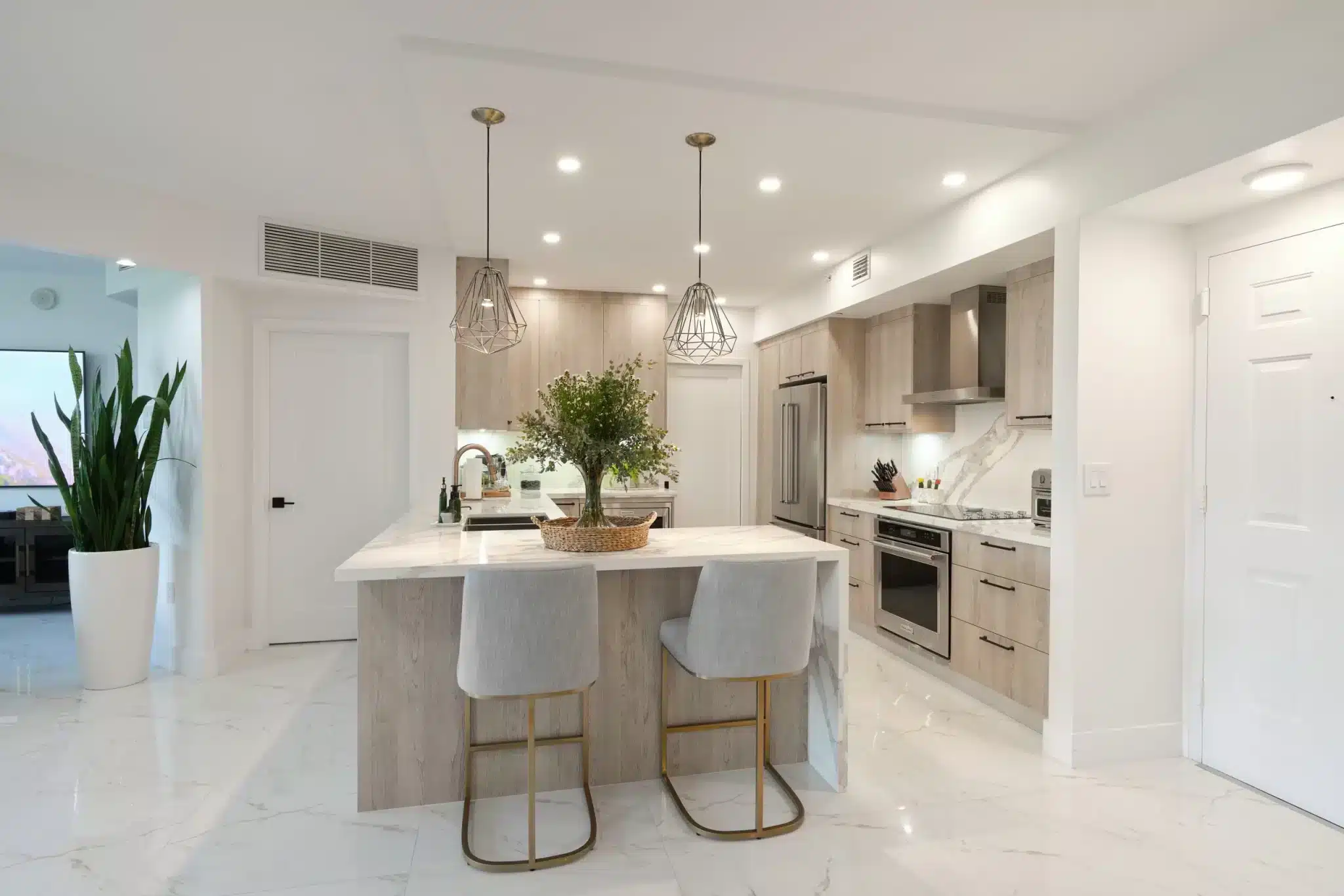 Modern kitchen with a large island, two bar stools, light cabinets, stainless steel appliances, and pendant lighting.
