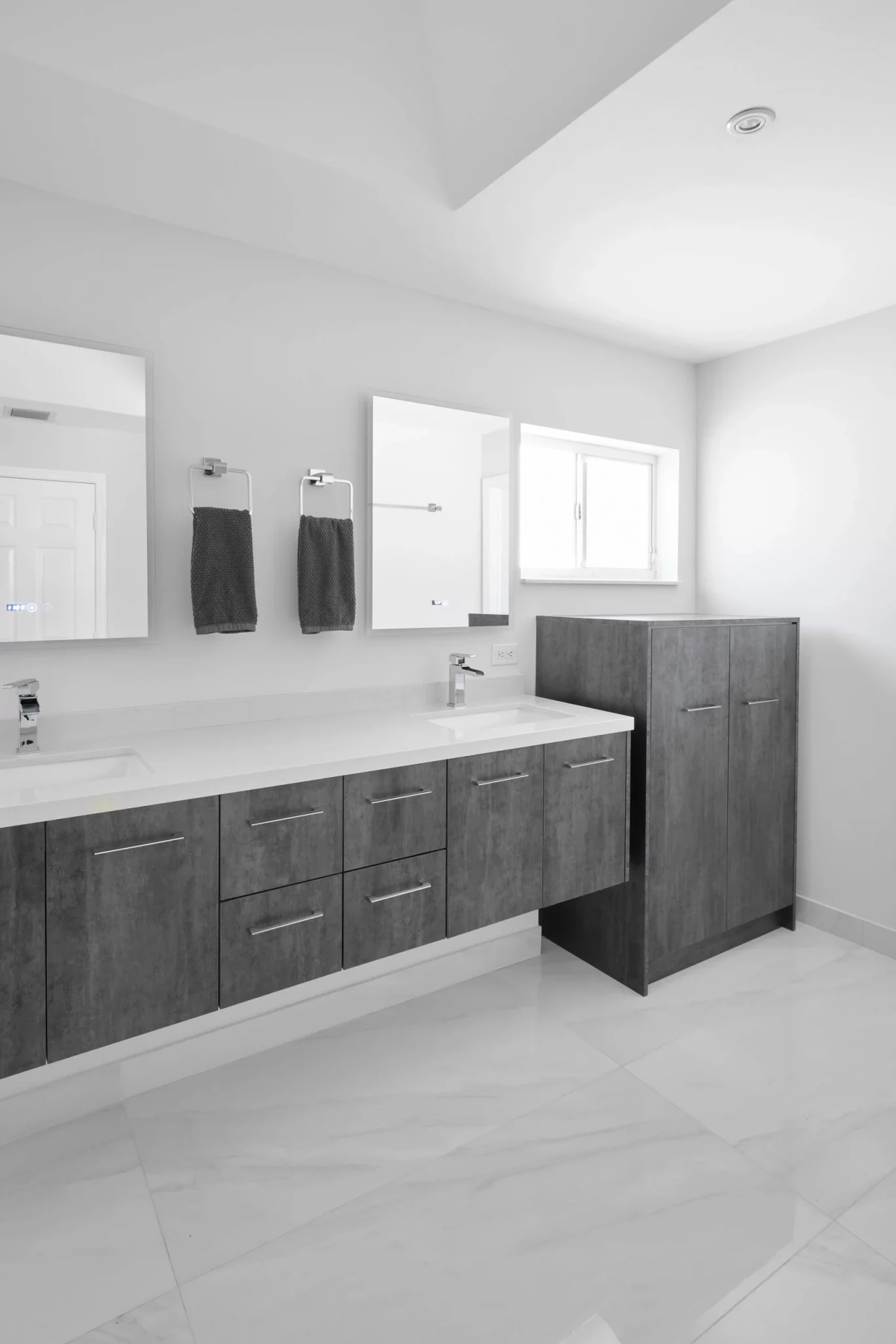 Modern bathroom featuring a double vanity with dark wood cabinets, two sinks, mirrors, and a tall storage unit.
