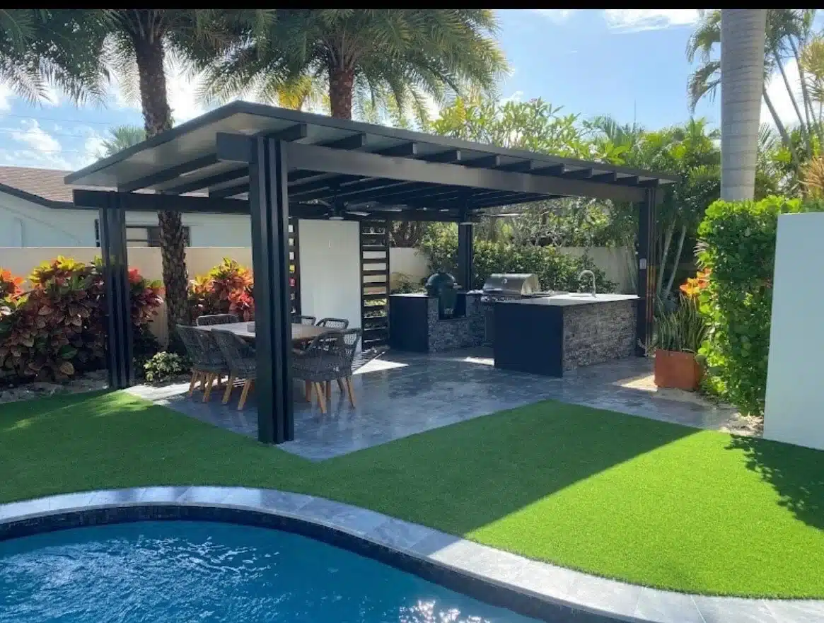 Black aluminum solid-roof pergola providing shade over an expansive outdoor kitchen and dining area next to a swimming pool.