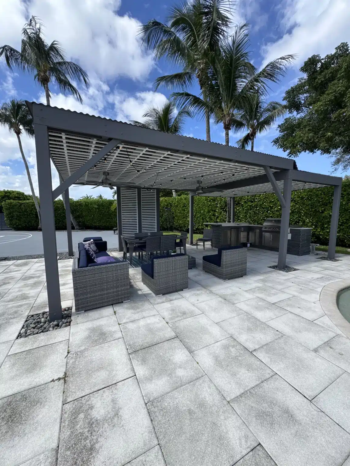 A professional pergola builder installed a large modern aluminum pergola with a light retractable fabric roof over a luxury outdoor lounge area.