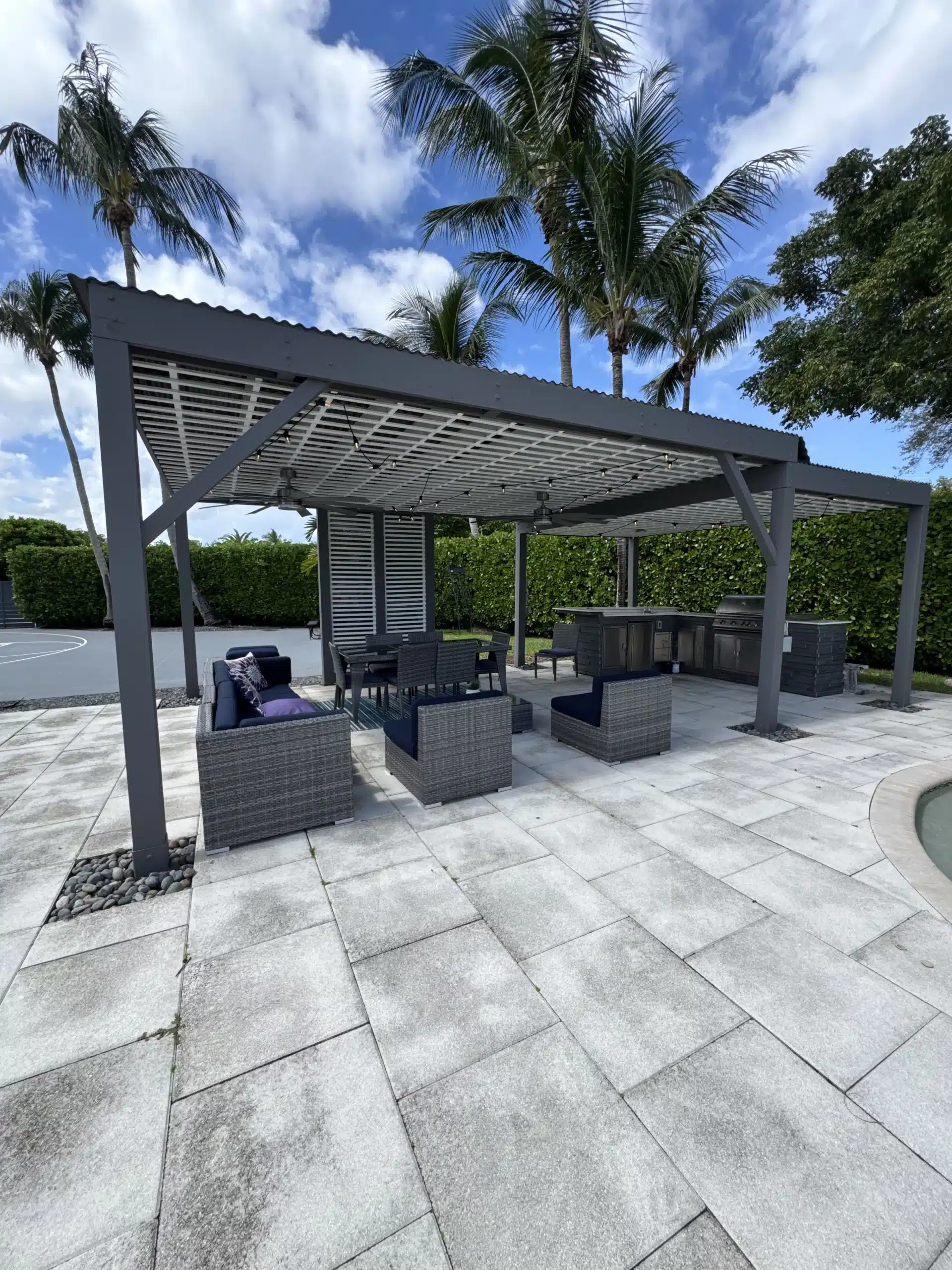 A professional pergola builder installed a large modern aluminum pergola with a light retractable fabric roof over a luxury outdoor lounge area.