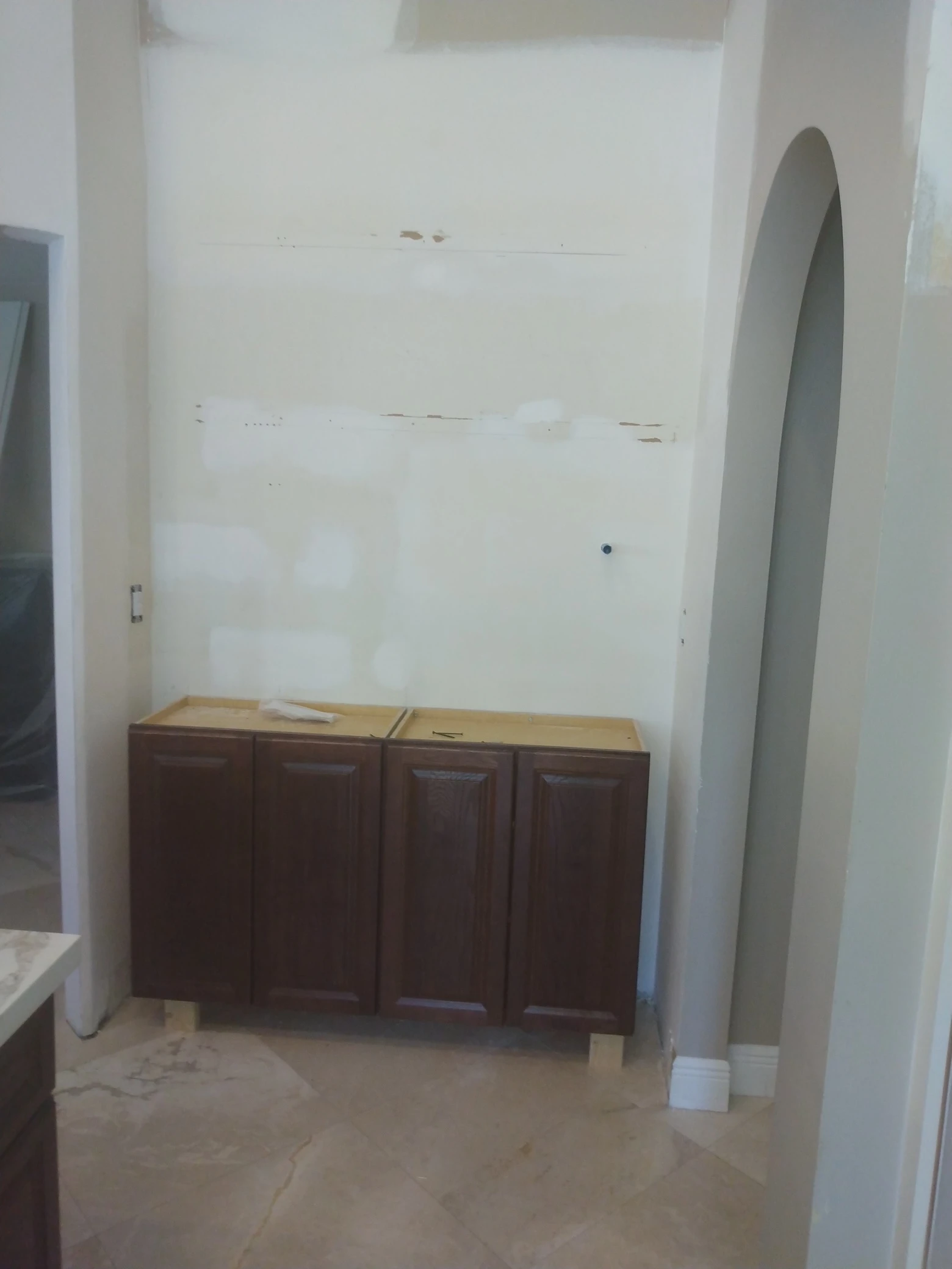 Before: Before photo of a custom coffee bar remodel in Plantation, FL, showing unfinished dark wood base cabinets, bare walls, and exposed wiring inside an arched niche