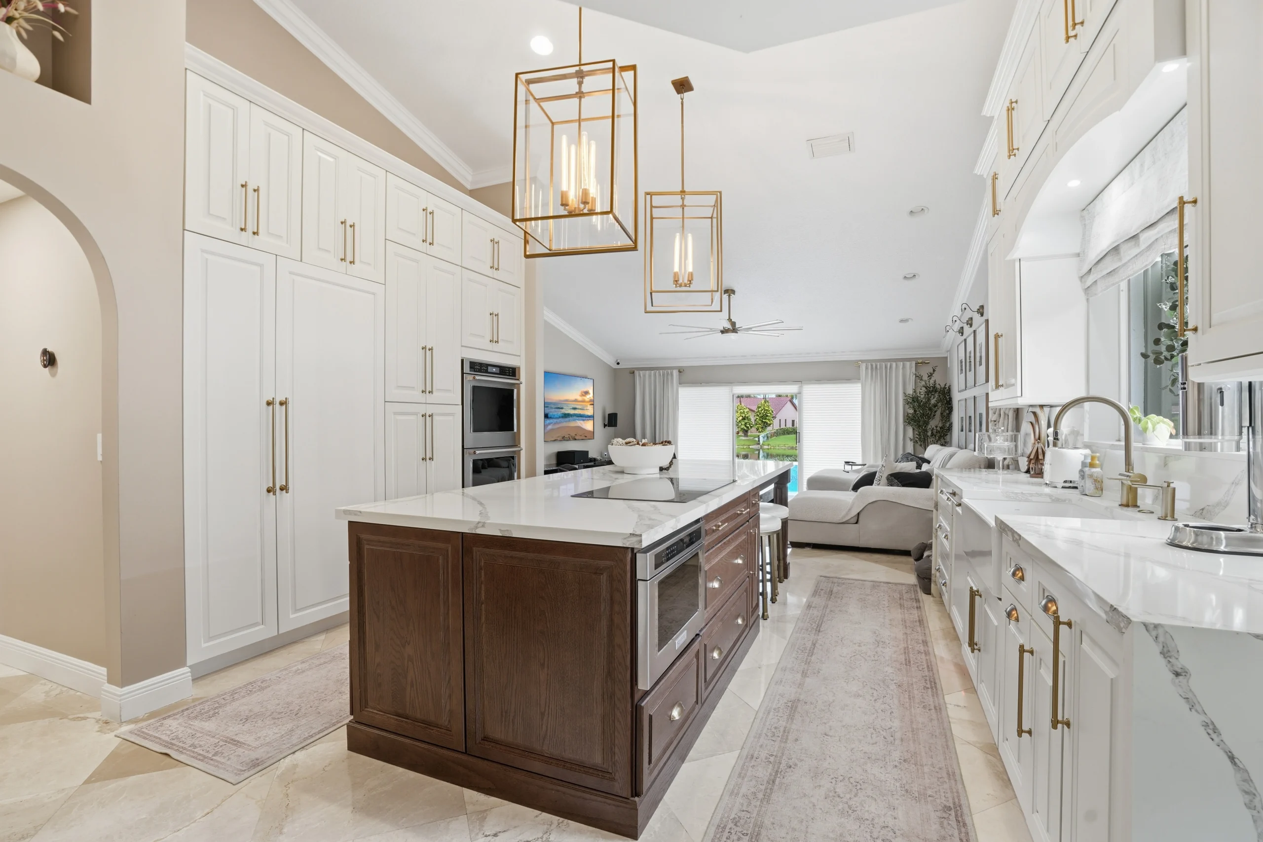 Luxury kitchen renovation in Plantation, FL featuring custom white cabinetry, a dark wood island, and gold pendant lights.