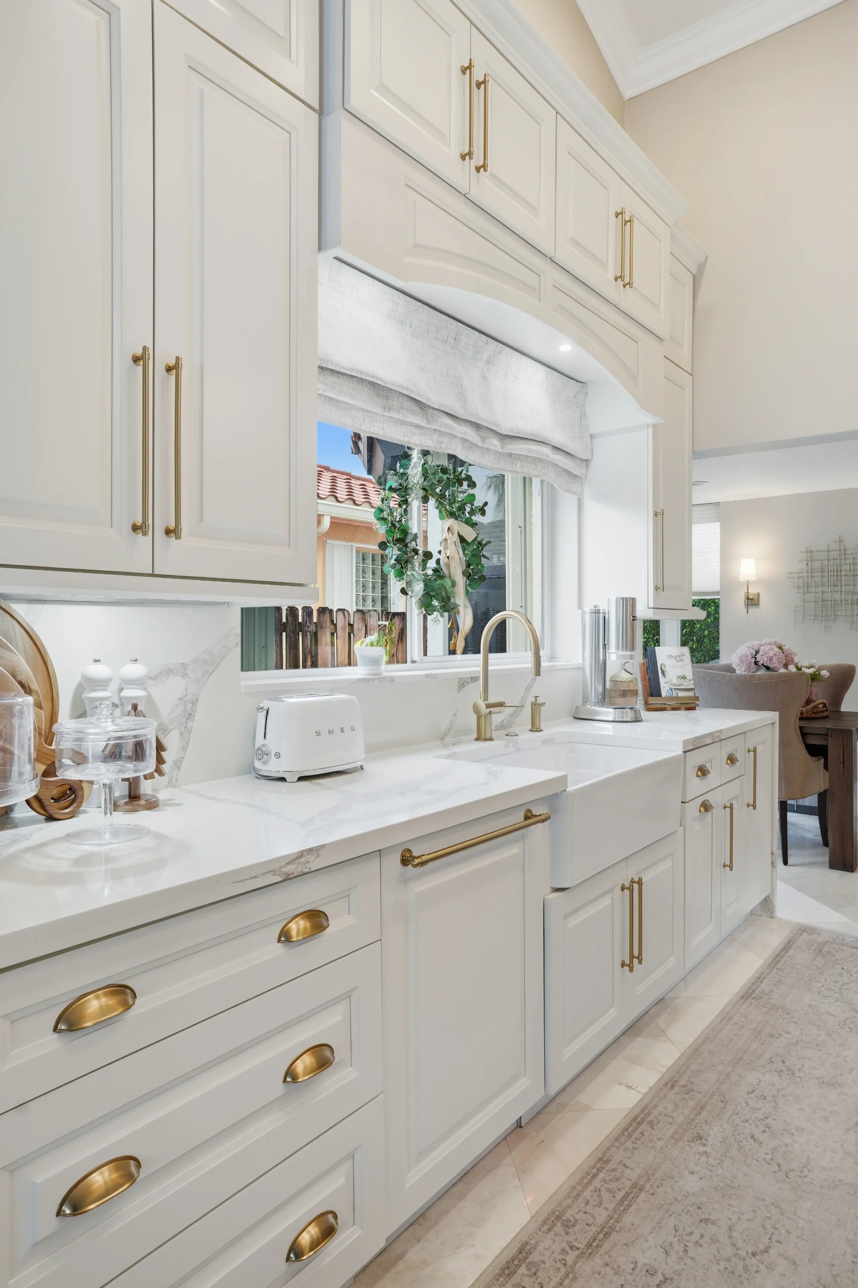 Elegant kitchen remodeling in Plantation FL featuring white cabinetry, brass hardware, and a marble farmhouse sink.